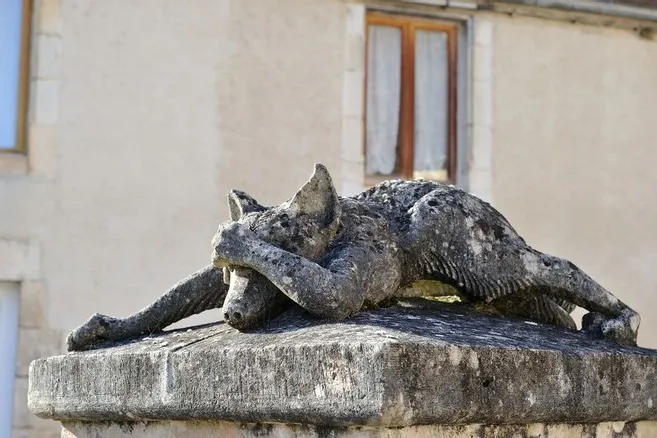 Statue en pierre d'un loup, allongé de tout son long sur le ventre. Une de ses pattes antérieures vient cacher son visage, car il est en train de pleurer.